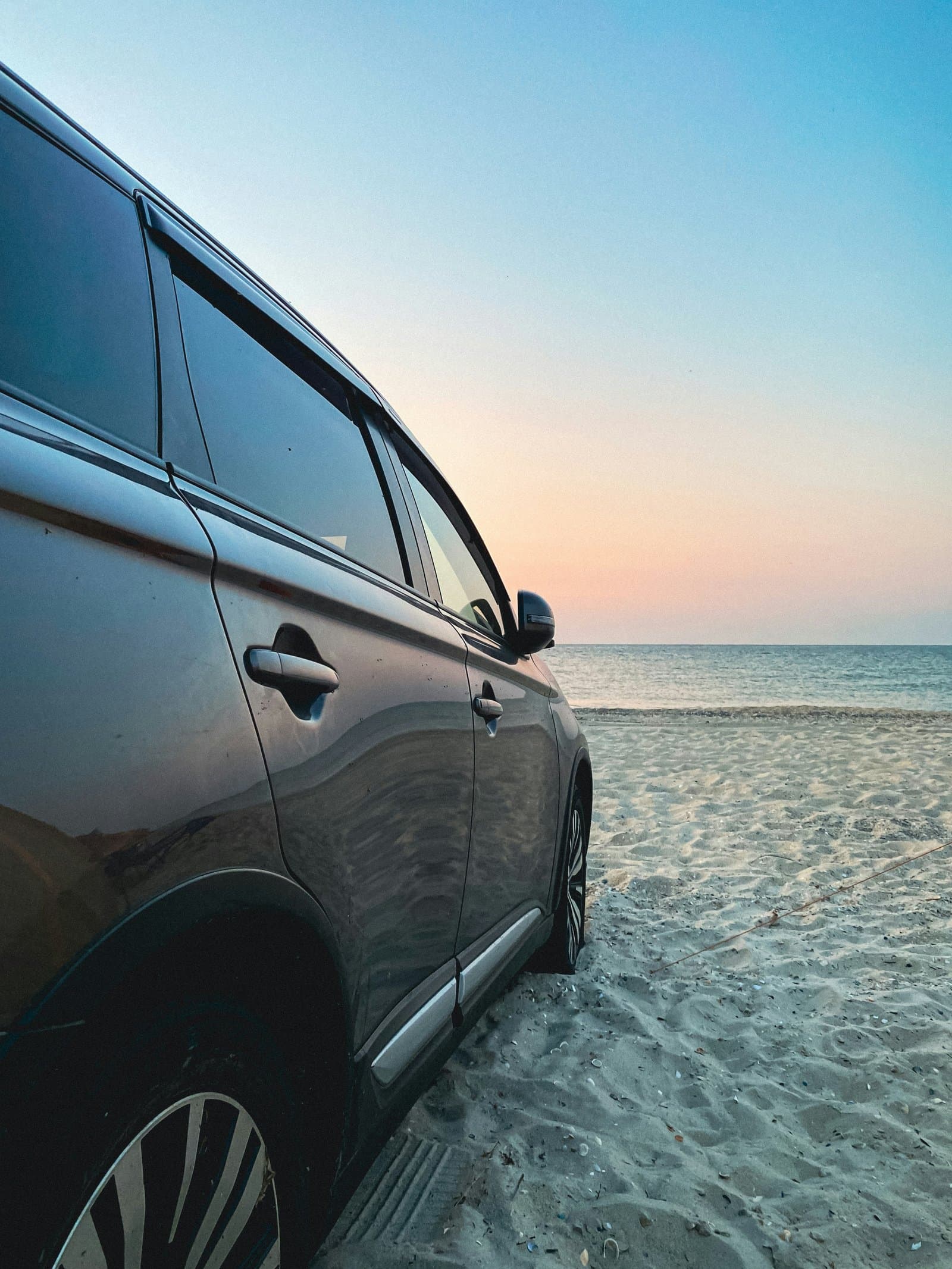 SUV parked on the sand at sunset, facing the sea