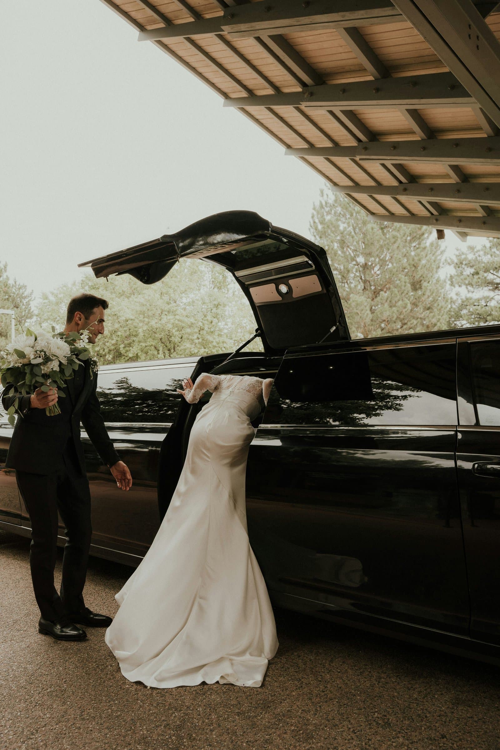 Bride stepping into a black limousine, the groom holding her bouquet