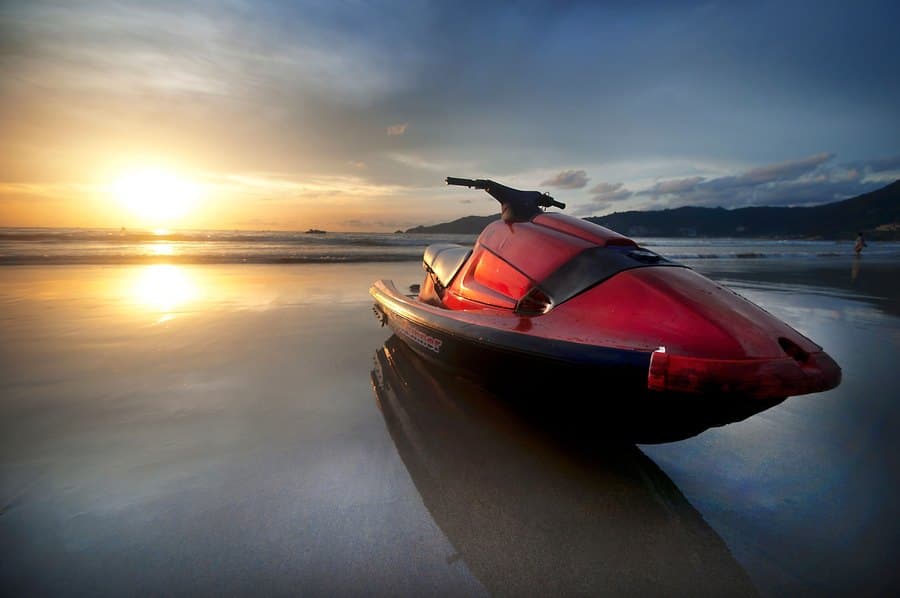 Red jet ski resting on wet sand at sunset